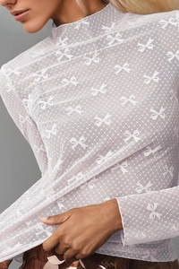 Close-up detail of white sheer lace mesh top with delicate bow pattern and polka dots