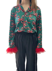 Detail of green satin pajama top with festive red bow print and faux feather cuffs