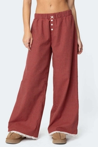 Dettaglio dei pantaloni a quadretti rossi con vita elastica, fiocco bianco e bordo in pizzo