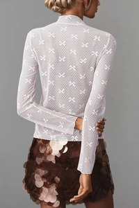 Macro shot of white long sleeve sheer mesh top featuring intricate butterfly lace patterns