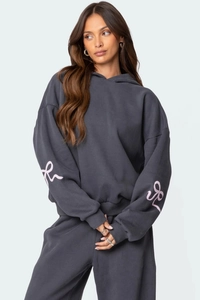 Détail de la manche d'un sweat gris avec imprimé nœud rose et poignets côtelés