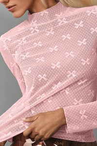 Detail of pink mesh top featuring bow and dot patterns with a high neckline design