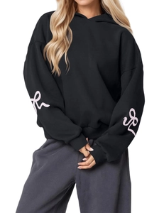 Detail of pink ribbon bow prints on sleeves of a black oversized long sleeve hoodie