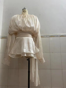 Detail of light beige puff sleeve top with pleated fabric and ruffled hem design