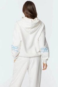Détail d'un sweat à capuche blanc avec broderie nœud bleu clair sur les manches