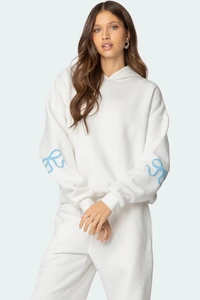 Détail de la manche d'un sweat blanc avec motif de nœud papillon bleu ciel en 3D
