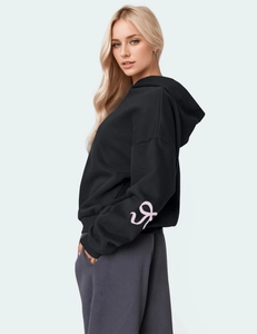 Detail of pink abstract logo on sleeve of black oversized fleece hoodie for women