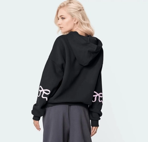 Back view of a black oversized hoodie featuring pink bow prints on the long sleeves