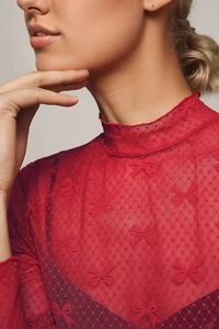 Detail of red sheer mesh top featuring intricate bow-knot lace patterns and a chic mock neck