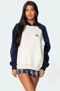Dettaglio del ricamo a fiocco blu su felpa con cappuccio beige e blu con maniche raglan
