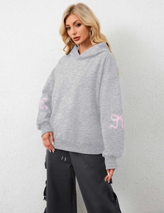 Detail of light grey oversized hoodie with pink ribbon bow patterns on the sleeves