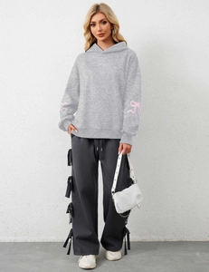 Detail of grey hoodie sleeves featuring pink ribbon bow prints and drawstring hood