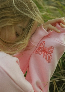 Close-up of red butterfly embroidery with SaaO letters on pink cotton sweatshirt sleeve