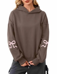 Detail of pink bow patterns printed on sleeves of a brown oversized hoodie