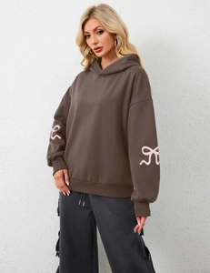 Close-up of pink bow graphics on sleeves of a loose coffee-colored hoodie