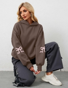 Detailed close-up of pink bow prints on the sleeves of a brown oversized hoodie