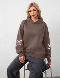 Detail of coffee brown oversized hoodie showing pink bow ribbon prints on the sleeves