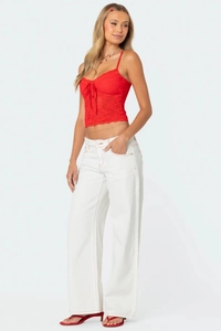 Détail d'un caraco en dentelle rouge avec nœud et pantalon blanc à surpiqûres rouges