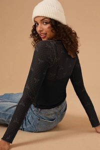 Close-up of black mesh long-sleeved top featuring an all-over bow pattern and sheer texture
