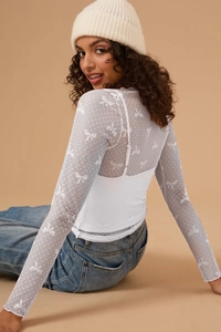 Detail of white mesh long-sleeve top with bow pattern and sheer texture on female model