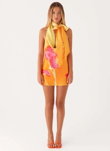 Détail d'une mini robe dos nu fleurie avec dégradé orange et nœud papillon à l'encolure