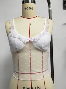 Détail d'un caraco blanc en dentelle avec nœud rose et maille à motifs de cœurs