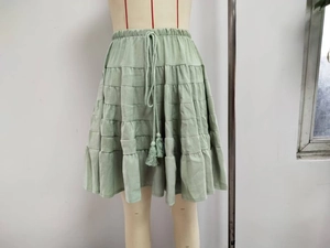 Detail of sage green tiered mini skirt with elastic drawstring waist and tassel charms