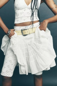 Detail of white bohemian embroidered lace set featuring layered ruffles and leather belt