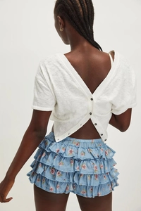 Detail of white open-back top with black buttons and floral tiered summer ruffle skirt