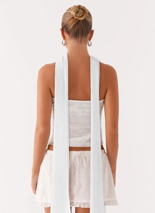 Detail of white satin halter top featuring long ribbons and delicate floral embroidery
