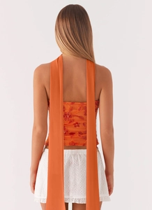 Detail view of orange mesh top with floral embroidery and elegant long back ribbons