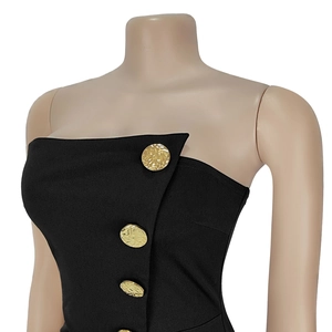 Detail of black strapless dress featuring diagonal cut and large gold textured buttons