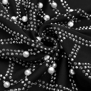Dettaglio di tessuto nero con strass argentati densi e decorazioni con perle bianche