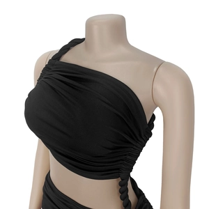 Détail du haut court noir asymétrique avec côtés froncés et bandoulière tissée élégante