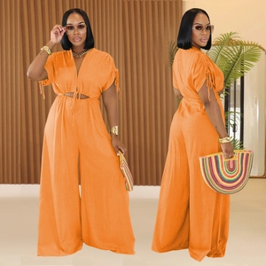 Detail of orange V-neck jumpsuit showing cutout waist, drawstring cuffs, and tie-up belt