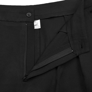 Close-up of black trousers showing button closure, metal zipper, and twill fabric texture