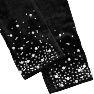 Gros plan d'une manche en velours noir ornée de perles blanches et de strass brillants