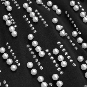 Macro shot of vertical white pearls and sparkling rhinestones on black dress fabric
