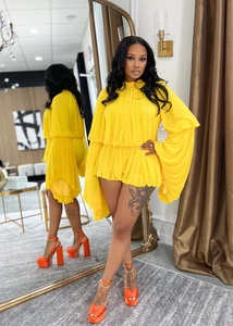 Detail view of bright yellow pleated romper with voluminous puff sleeves and ruffled hem