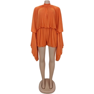 Detail of bright orange romper featuring pleated fabric and dramatic cape-style long sleeves