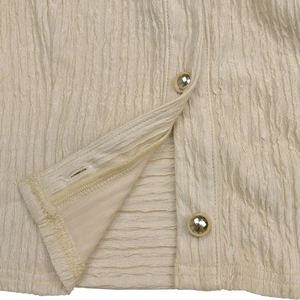 Detail view of beige pleated fabric with textured finish and decorative gold buttons
