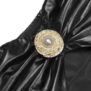 Detailed close-up of a golden round button with a pearl on black glitter pleated fabric