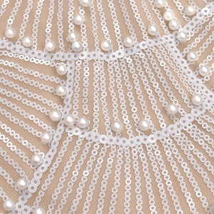 Close-up of sparkling white sequins and pearl embroidery on beige mesh fabric