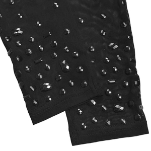 Dettaglio dell'abito in rete nera con vari strass neri e borchie di forme geometriche