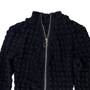 Detail of bubble-knit black texture with golden ring zipper on a minimalist jacket