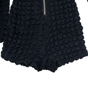 Close-up of black popcorn fabric texture and golden metal zipper on a long sleeve romper