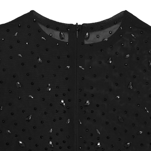 Dettaglio dell'abito in rete trasparente con paillettes nere, gemme e zip invisibile