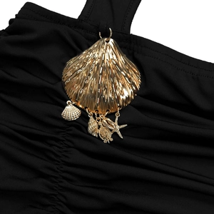 Detail of black pleated fabric with a golden scallop shell and starfish charm pendant