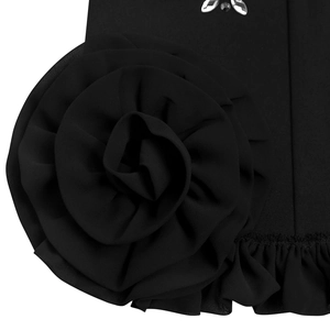 Détail de la robe noire élégante montrant une grande fleur 3D et des strass étincelants