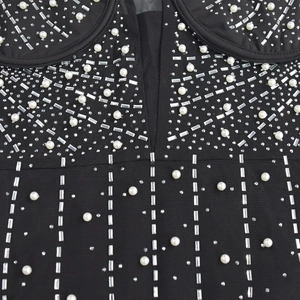 Détail de robe en maille noire avec perles blanches et ornements en strass argentés